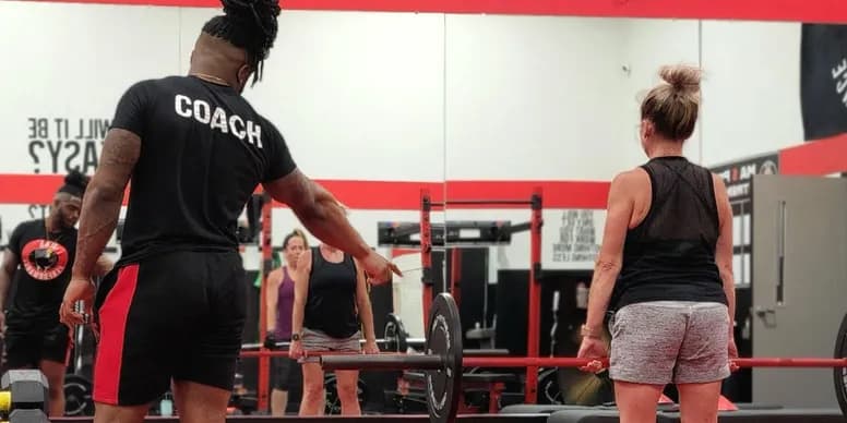 Coach guiding a client through a barbell lift at MA5 Performance